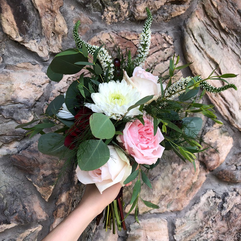 holding a bouquet of white, red, and rose-pink flowers and leaves, beautiful hardscape as background