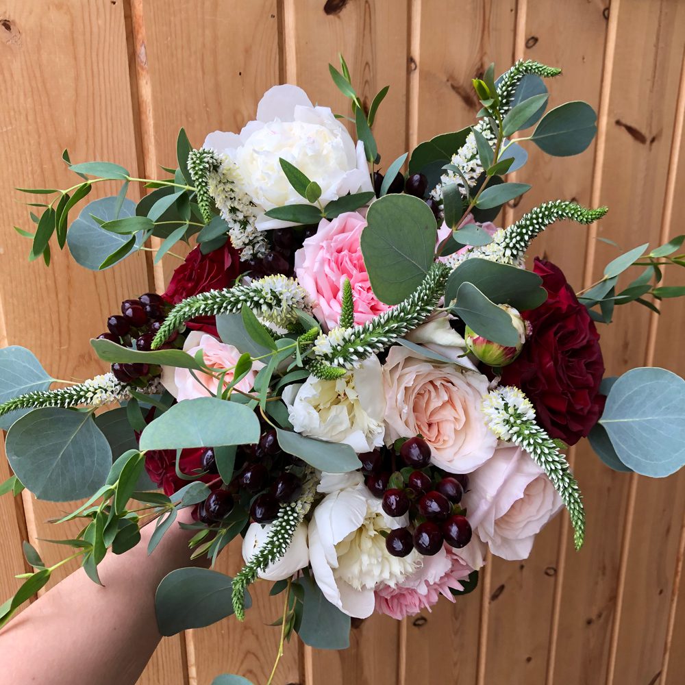 bouquet of white, red, and rose-pink flowers and leaves, wooden planks as background