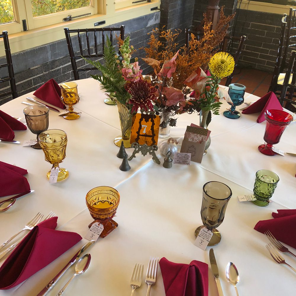 table settings with fall-themed flowers arrangement and different colors of wine glasses