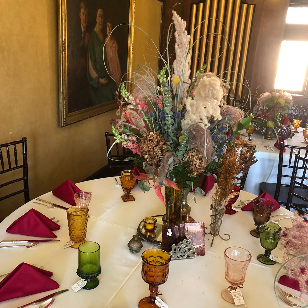 table settings with fall-themed flowers arrangement at the center and different colors of wine glasses for table four