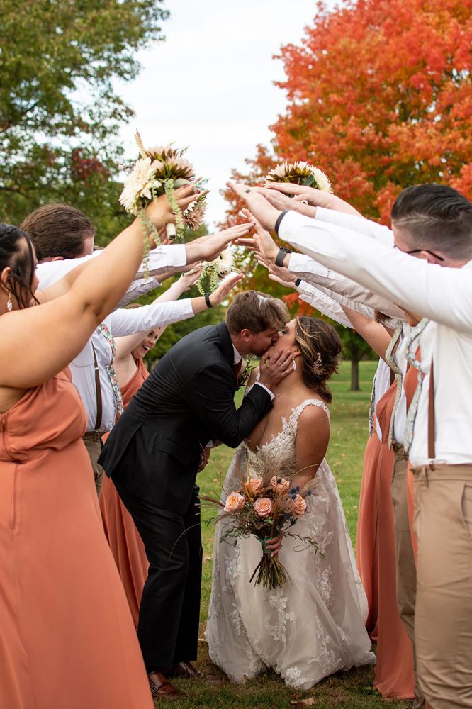 kissing newlywed while the bridesmaid and bridegroom are raising their hands