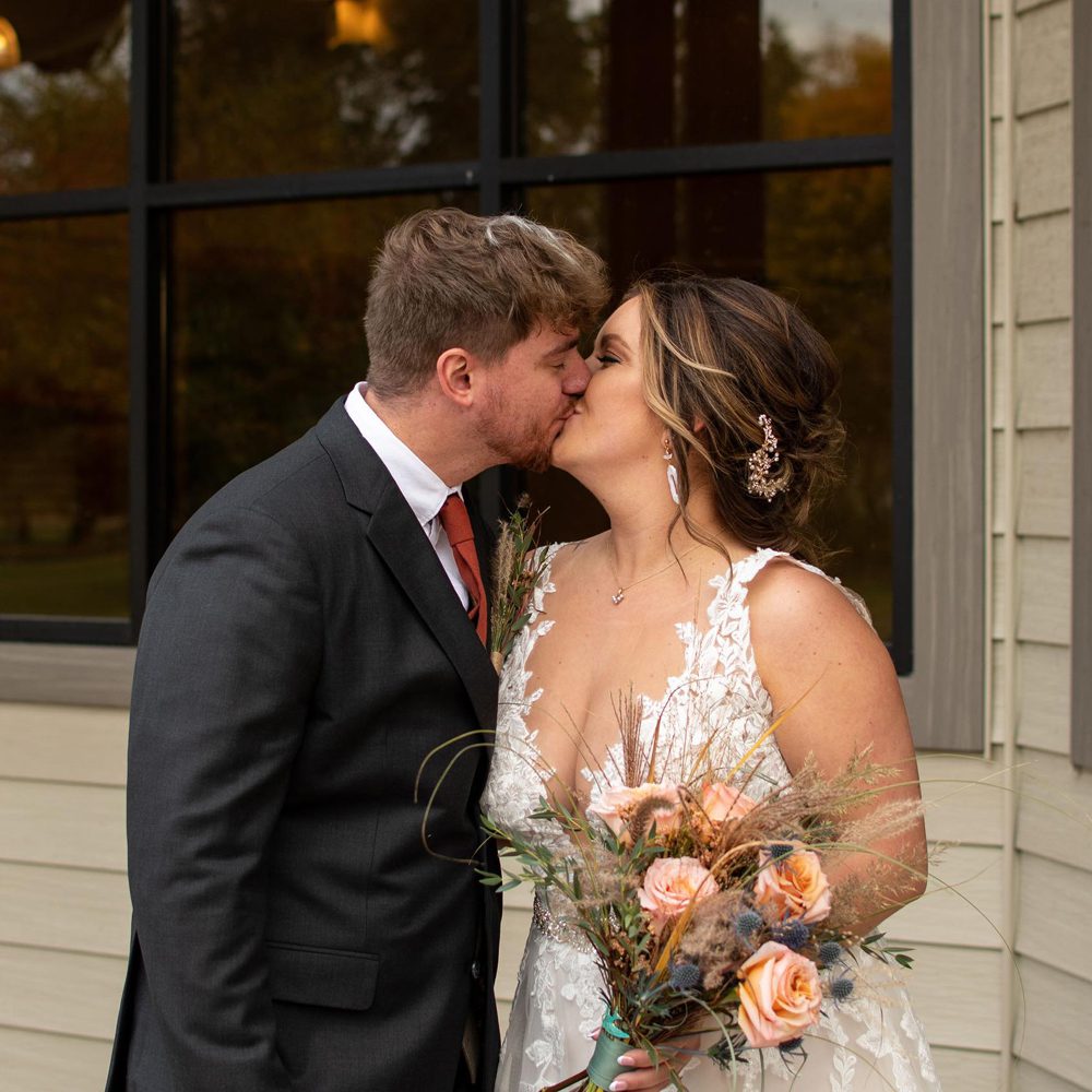 kissing couple while the bride is holding her bouquet
